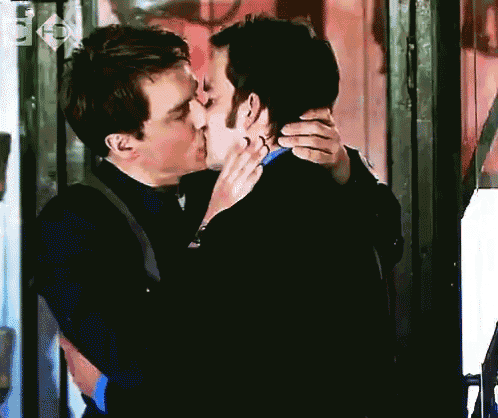 two men kissing in front of a sign that says ' fox ' on it