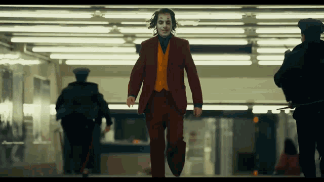 a man dressed as the joker is walking down a hallway with police behind him .