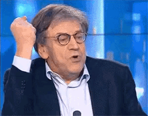 a man in a suit and glasses is making a funny face while sitting in front of a microphone .
