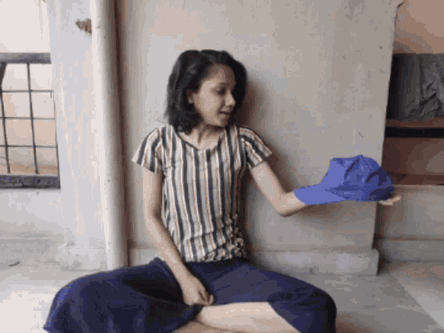 a woman in a striped shirt is sitting on the floor holding a blue hat with the letter a on it