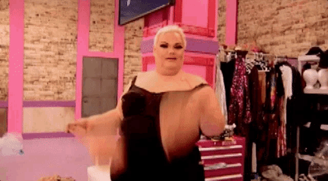 a woman in a black dress is standing in a room with pink walls and clothes .