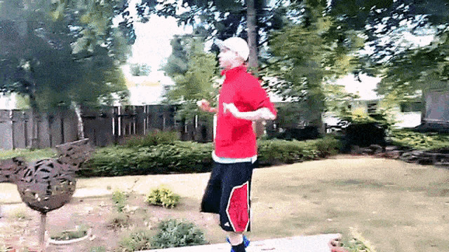 a man in a red shirt and black shorts is standing in a yard