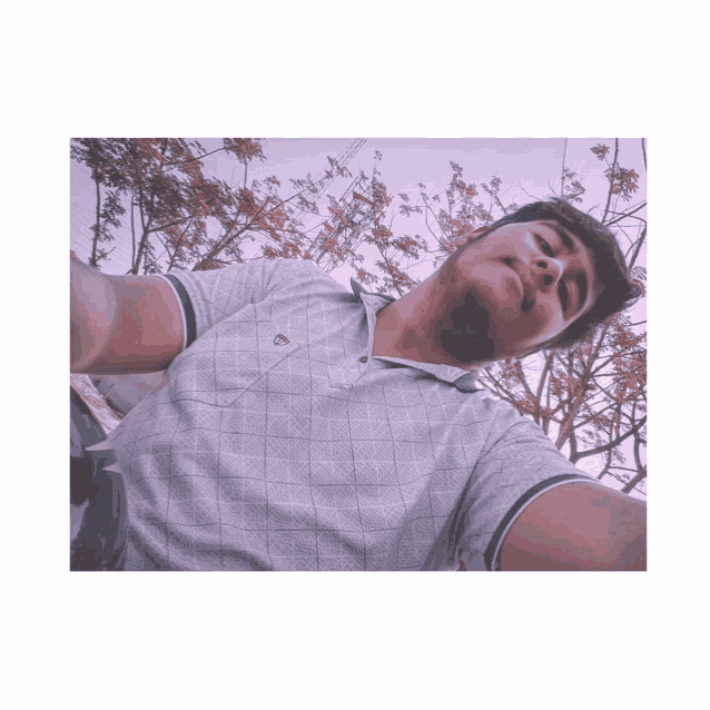 a man taking a selfie in front of a tree wearing a polo shirt