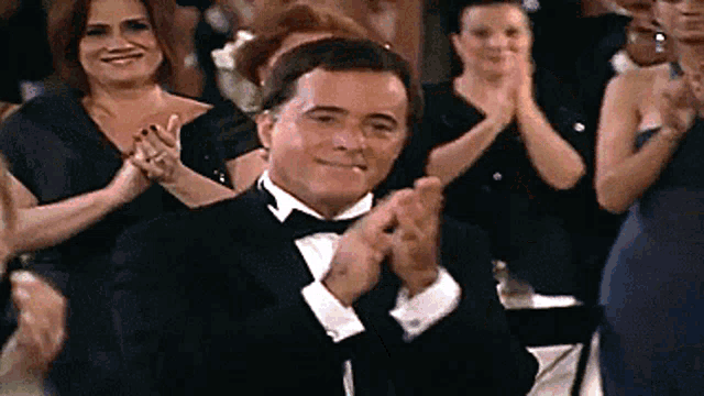 a man in a tuxedo is clapping in a crowd