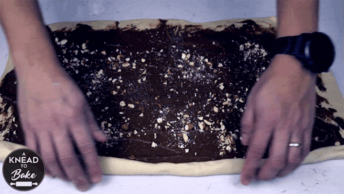 a person is spreading chocolate and nuts on a piece of dough that says knead to bake on it
