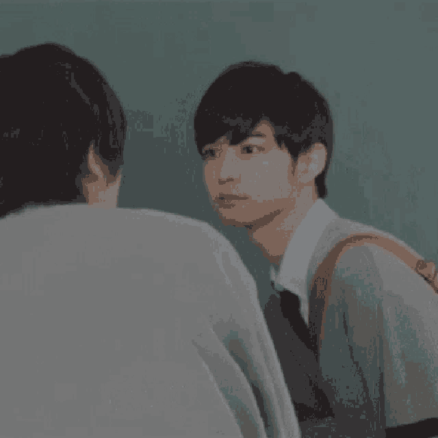 a man in a suit and tie is looking at another man in a classroom .