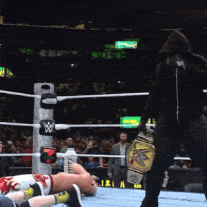 a man in a black hoodie stands in a wrestling ring with a w on the ropes
