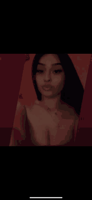 a woman without a shirt is taking a selfie in front of a red wall .
