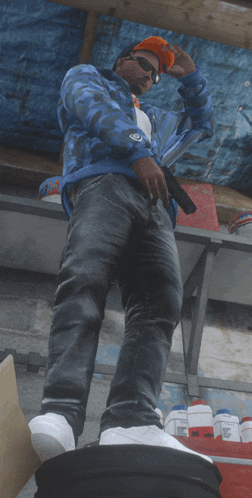 a man in a blue jacket and orange hat is standing on a pile of barrels