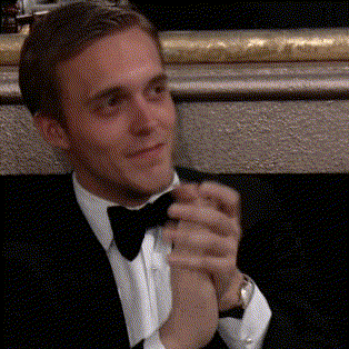 a man in a tuxedo and bow tie holds his hands together