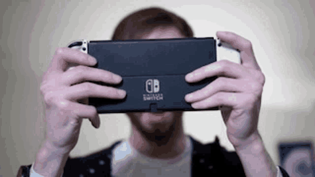 a man is holding a nintendo switch in front of his face .