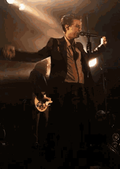 a man in a suit is singing into a microphone while holding a guitar .