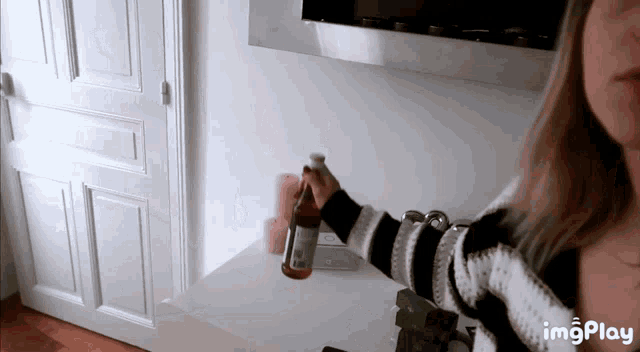 a woman in a striped sweater is holding a bottle of wine in her hand with imgplay in the corner
