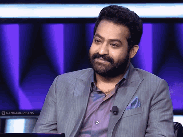 a man with a beard is sitting in front of a microphone and a sign that says nandamurifans on it