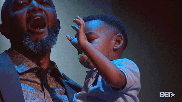 a man is holding a baby with a pacifier in his mouth and the bet logo is visible in the corner