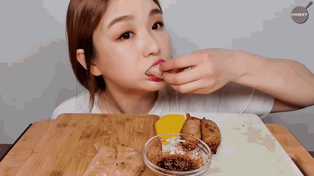 a woman is eating food on a cutting board with the word hamzy on the bottom right