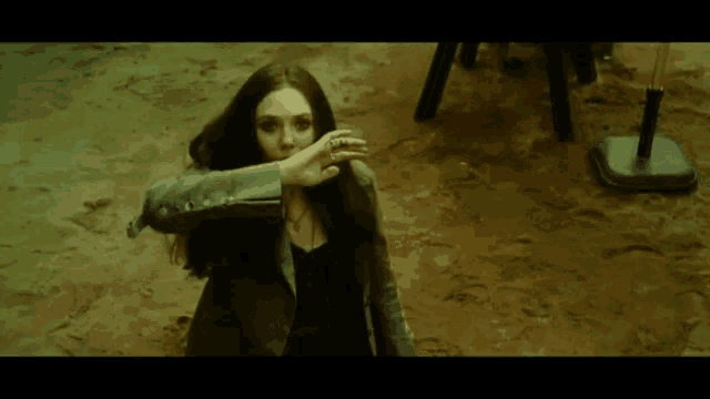 a woman with long dark hair is standing in the dirt with her hand on her face