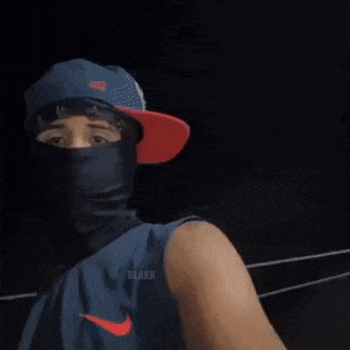 a man wearing a hat and a mask is standing in front of a car .