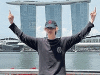 a man is standing in front of a body of water with his arms outstretched and giving the middle finger .