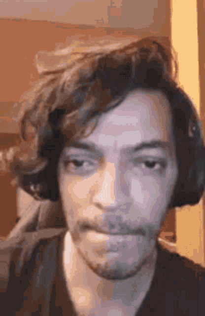 a man with a beard and long hair is wearing headphones and making a funny face .