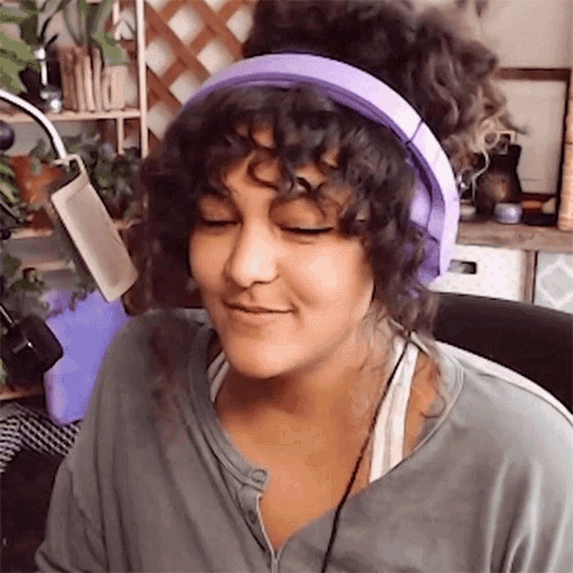 a woman with curly hair is wearing purple headphones and smiling while sitting in front of a microphone .