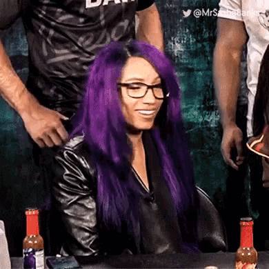 a woman with purple hair is wearing glasses and a leather jacket .