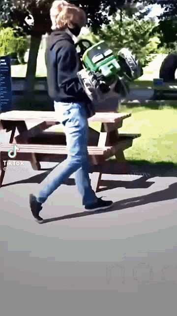 a man wearing a mask is carrying a green chair while walking down the street .