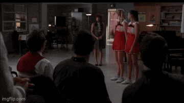 a group of cheerleaders are standing in a room with a man in a wheelchair .