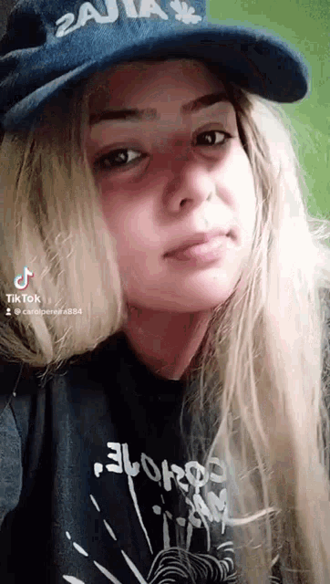 a young woman wearing a hat and a t-shirt is looking at the camera .