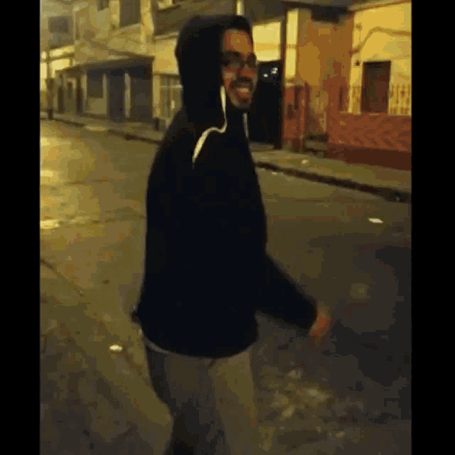 a man wearing a hoodie and glasses is walking down a street