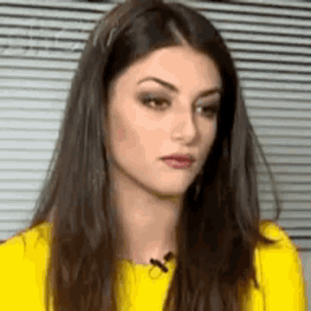 a woman with long dark hair is wearing a yellow shirt and a microphone .