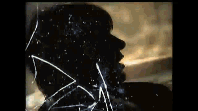 a silhouette of a man 's face is behind a broken glass .