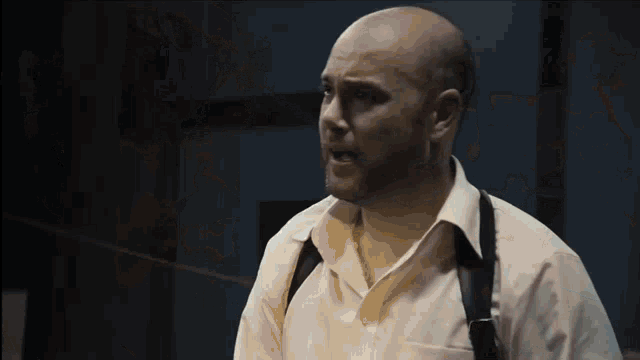 a bald man in a white shirt and suspenders looks angry