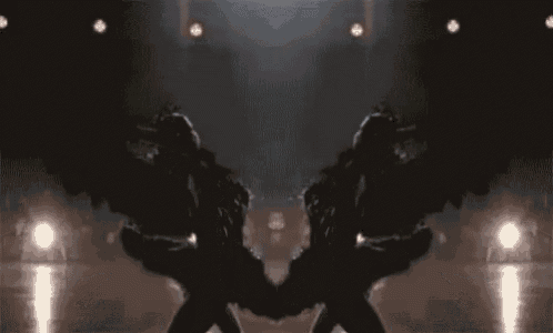 a couple of people with black wings are standing next to each other on a stage holding hands .
