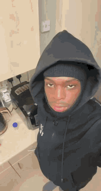 a man wearing a black hoodie and a black beanie is standing in front of a phone