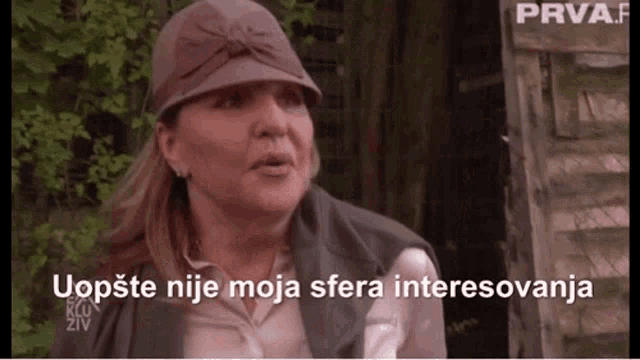 a woman wearing a hat and a vest with the words uopste nije moja sfera interesovanja written below her
