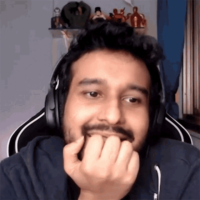 a man with a beard and headphones is sitting in a chair with his hands on his chin .