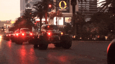 a group of monster trucks are driving down a street in front of a sign that says cirque du soleil