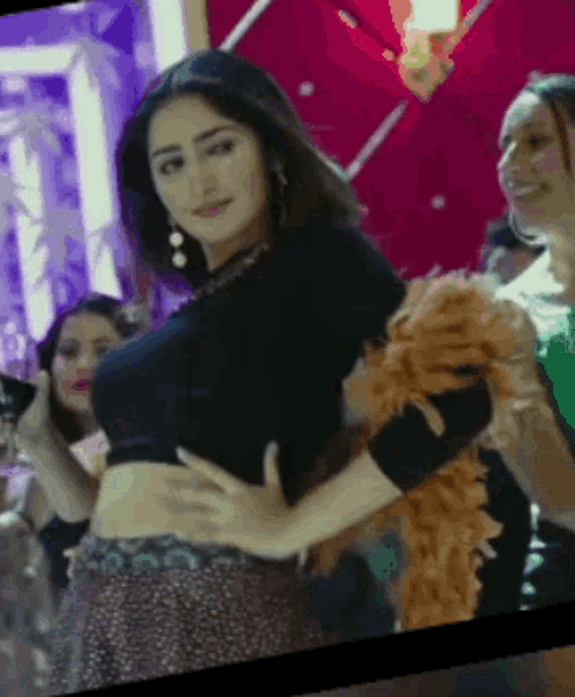 a woman in a black crop top is dancing in a room with other women