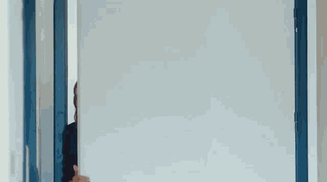 a woman is peeking out from behind a door .