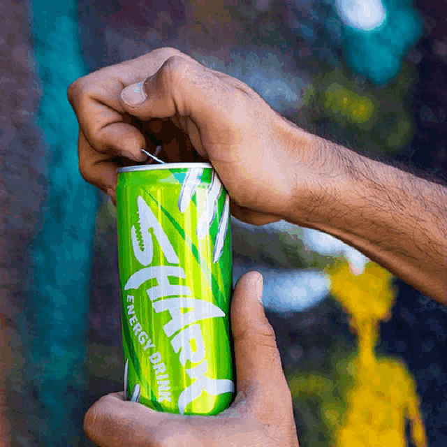 a person is holding a can of shark energy drink in their hand
