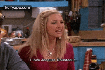 a woman is sitting at a table with a man in a kitchen and says i love jacques cousteau .