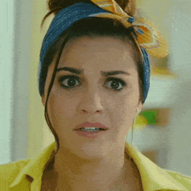 a woman wearing a blue headband and a yellow shirt looks surprised
