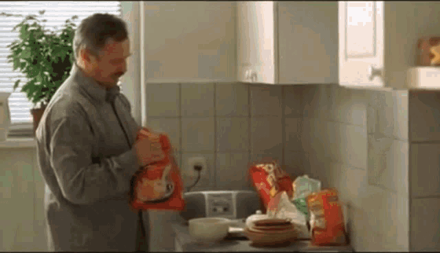 a man is standing in a kitchen holding a bag of doritos chips