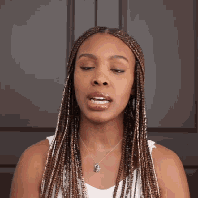 a woman with braids is wearing a white tank top and a necklace