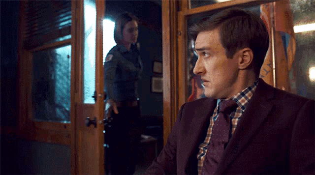 a man in a suit and tie stands in front of a woman in a police uniform