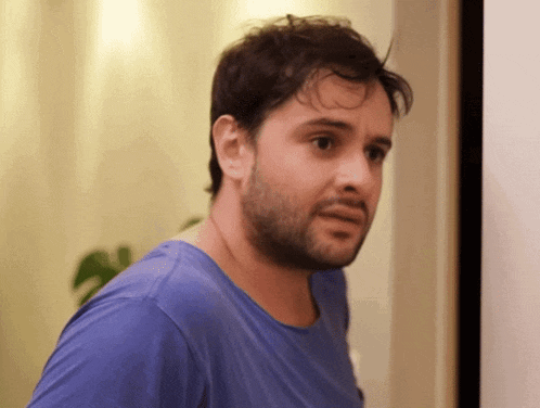 a man with a beard wearing a blue shirt looks to the side