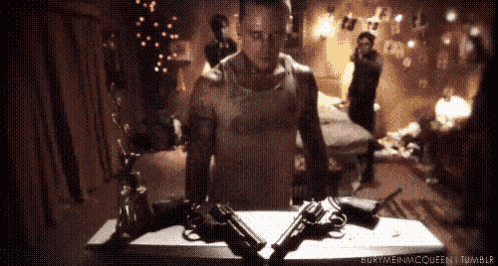 a man is standing next to two guns on a table in a room .