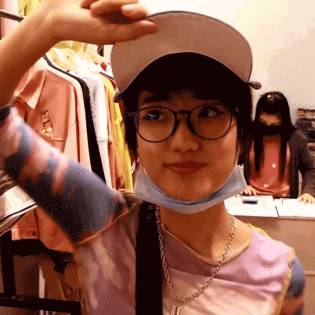 a woman wearing glasses and a mask is standing in front of a clothes rack