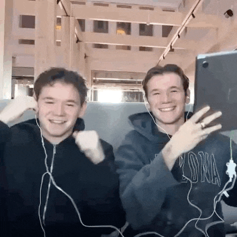 two young men are sitting next to each other wearing headphones and looking at a tablet .